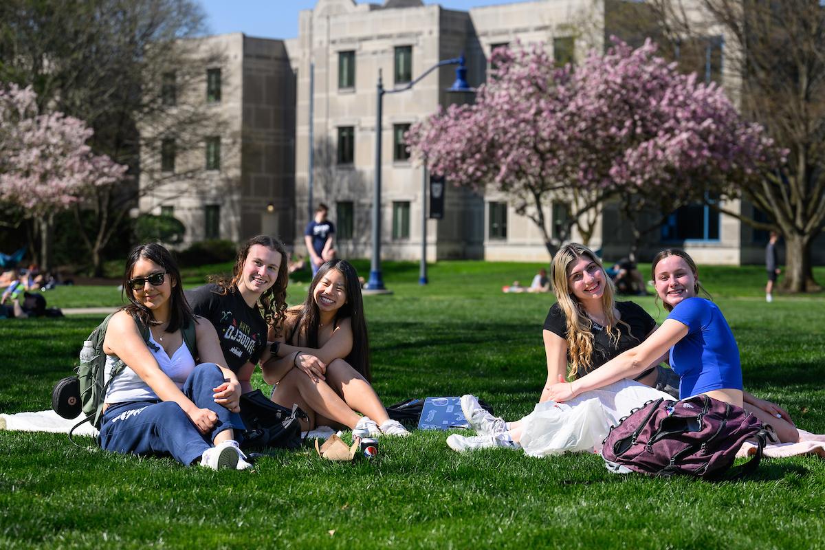 A group of students sits outdoors on grass, smiling.